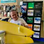 Joe Roper assessing a yellow surfboard that has another board's fin stuck in it from a bad wipeout.