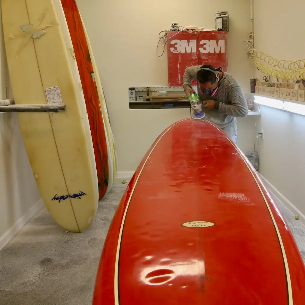 Man repairing and restoring a red vintage Velzy surfboard.