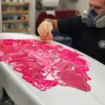 Jojo Roper wearing a work mask while working on a pink swirl surfboard color job at his factory.